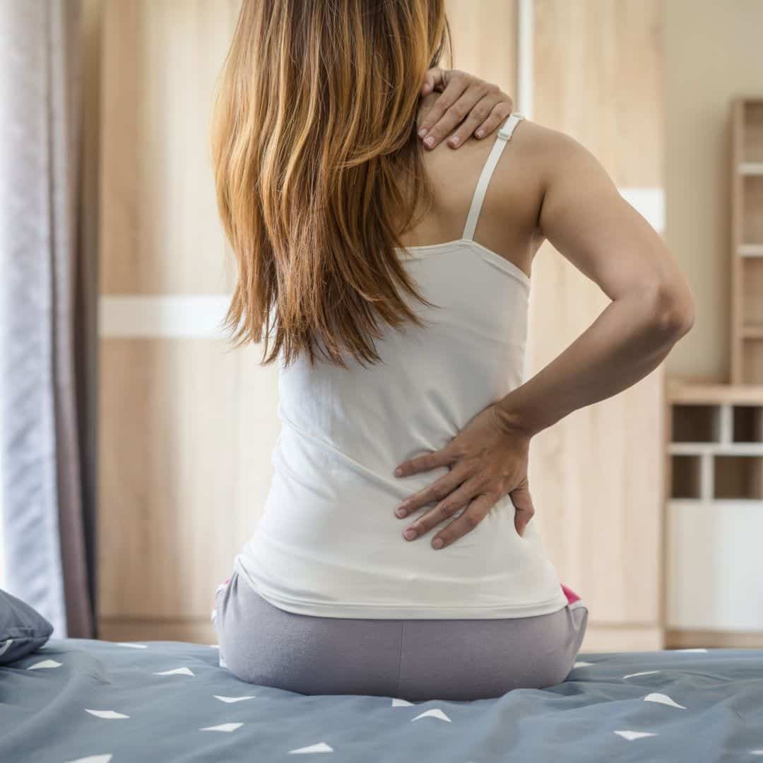 A woman experiencing neck pain and back pain while lying in bed.