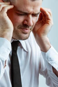 Stressful businessman suffering from headache, with his eyes shut holding hands to his napes. Close-up studio portrait