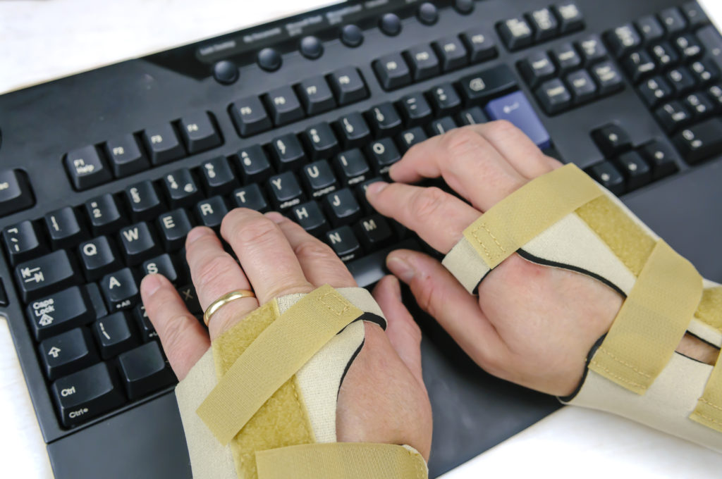 Man with Carpal Tunnel Syndrome, Rheumatoid Arthritis or Osteoarthritis and wearing wrist splints using a computer keyboard 