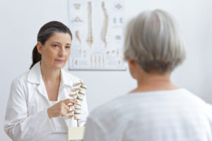 doctor of orthopedics showing her senior patient a slipped disk on a backbone model