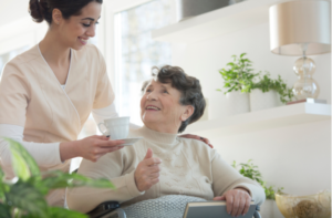 Friendly volunteer giving cup of tea to happy senior woman in nursing home