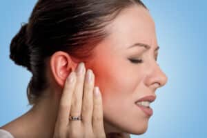 A profile shot of a woman holding her jaw and experiencing facial pain from trigeminal neuralgia