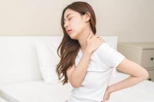 Woman sitting on bed holding her neck in severe pain, needing Cervical Artificial Disc Replacement